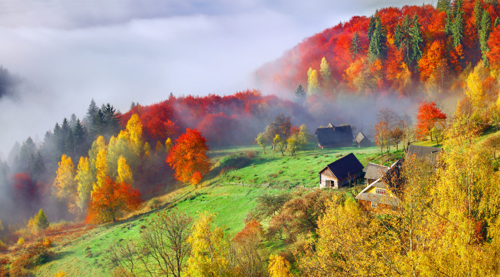 Colorful autumn landscape in the mountain village. Foggy morning